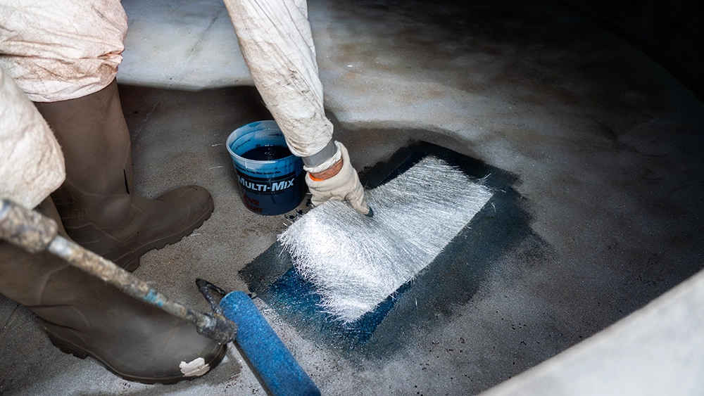 Person in protective gear installing fiberglass laminate on corroded area.